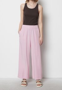 Top senza maniche marrone abbinato a pantaloni larghi rosa chiaro con vita elastica e tasche laterali. Tessuto di morbida consistenza.