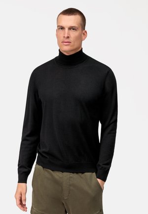 Zwarte coltrui gemaakt van een zachte stof, met lange mouwen en een getailleerd ontwerp, gecombineerd met olijfgroene shorts.