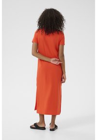 Orange midi kjole med korte ærmer, der har sideslids og en afslappet pasform. Bæres med sorte slidesandaler.