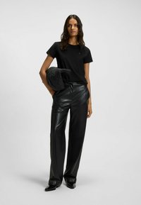 Schwarzes T-Shirt mit kurzen Ärmeln und subtiler Logo, kombiniert mit hochtaillierten schwarzen Kunstlederhosen und einer schwarzen gesteppte Jacke.