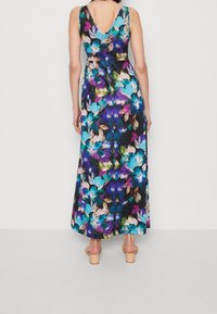 Robe maxi florale avec dos en V, couleurs vives incluant le bleu et le violet, avec une silhouette fluide et une longueur jusqu'aux chevilles.