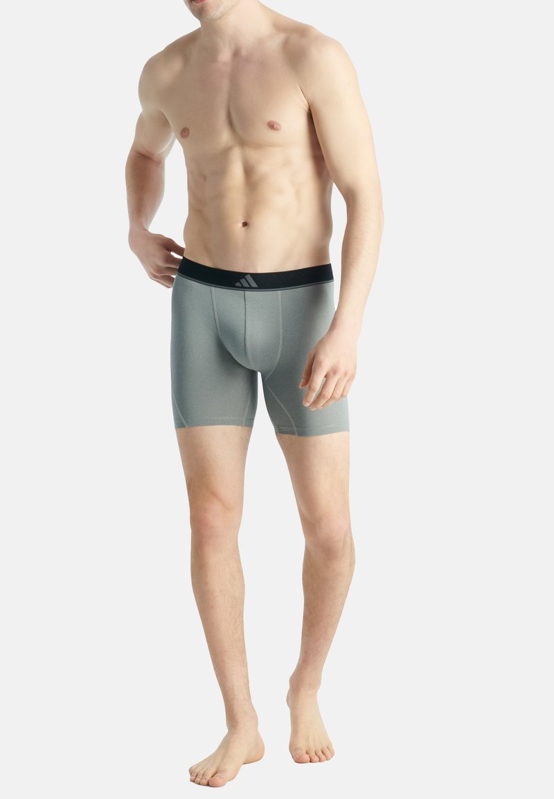 Grå boxer shorts med en svart elastisk midjeband som har en logotyp, slät textur och en åtsittande design som når mitt på låret.