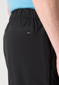 Zwarte lichtgewicht shorts met een elastische tailleband, voorzien van een zijzak en subtiele Calvin Klein branding nabij de tailleband.