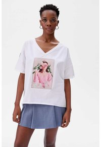 Witte V-hals t-shirt met een opvallende roze graphic featuring bloemen en een model. Gekozen in combinatie met een blauwe plooienrok. Van katoen.