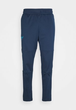 Marineblaue, schmal zulaufende Sporthose mit elastischem Bund und Nahtdetails an den Knien, dargestellt auf weißem Hintergrund.