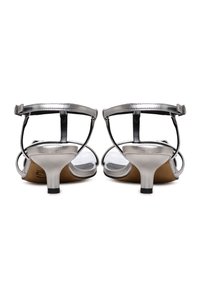 Stříbrné metalické sandály na podpatku s úzkým páskem kolem kotníku, otevřenou špičkou a krátkým, robustním podpatkem. Hladká textury a elegantní design.