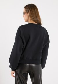 Felpa nera dal taglio ampio, con polsini e orlo a costine. Realizzata in materiale morbido, presenta spalle scese e una texture liscia.