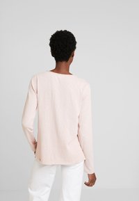 Maglietta a maniche lunghe rosa realizzata in un tessuto morbido e testurizzato con una vestibilità rilassata, caratterizzata da un colletto arrotondato e dettagli di cucitura discreti sull'orlo.