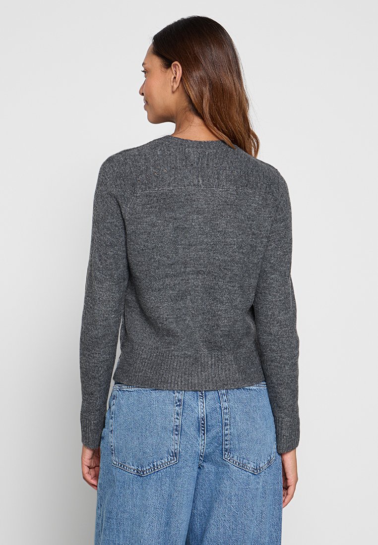 Grijze gebreide trui met een geribde zoom en boorden, voorzien van een ronde halslijn en een gestructureerde achterkant. Gecombineerd met hoge blauwe jeans.