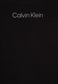 Černá látka s logem "Calvin Klein" v stříbrném písmu. Materiál vypadá hladce a je trochu elastický s jednoduchým designem.