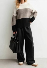 Pletený svetr s blokovým vzorem v krémové, šedohnědé a černé barvě, doplněný černými kalhotami s širokými nohavicemi a černou kabelkou. Bílé boty.