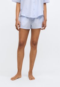 Σετ πιτζάμες ανοιχτού γαλάζιου χρώματος με κοντά μανίκια και λεπτές λευκές ρίγες. Το πάνω μέρος είναι φαρδύ, ενώ τα σορτς είναι λεία και καλοραμμένα.