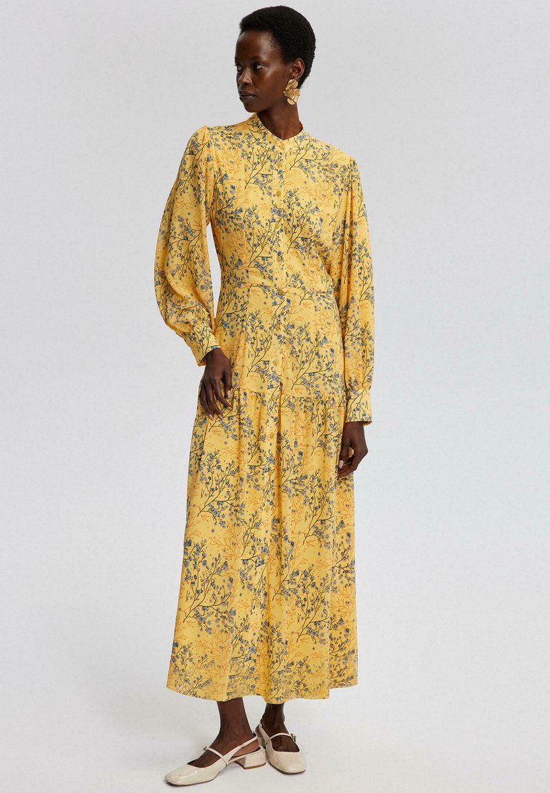 Gelbes Blumenmusterkleid mit langen Puffärmeln, plissiertem Rock und Stehkragen. Hat blaue Blumenmuster auf einem strukturierten Stoff.