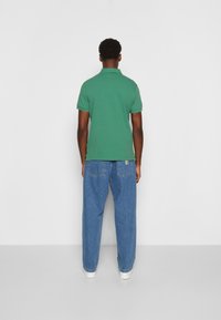 Green polo shirt with short sleeves, paired with loose-fitting blue jeans and white sneakers, viewed from the back.