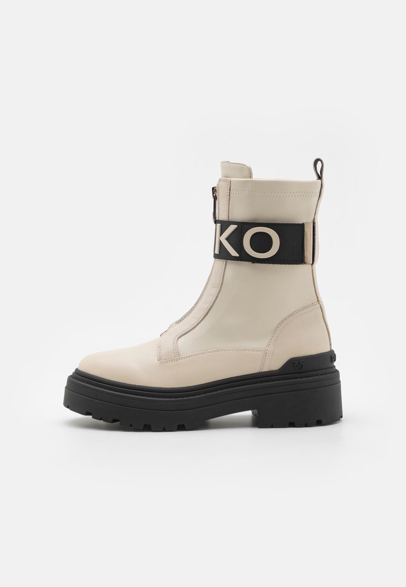 Bottes chelsea beige en cuir lisse, avec une semelle épaisse noire, une fermeture éclair latérale et une sangle noire avec des lettres blanches.