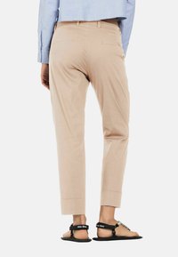 Beige broek met een taps toelopende snit, zijzakken en opgerolde zoom, gecombineerd met zwarte sandalen met een decoratieve band.