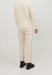 Beige stickad tröja med långa ärmar kombinerad med ljusbeige uppvikta byxor och svarta läderskor. Slät textur, avslappnad passform.