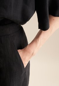 Czarna lniana bluzka z luźnymi rękawami, połączona z czarnymi materiałowymi spodniami z bocznymi kieszeniami. Gładka faktura i minimalistyczny design.