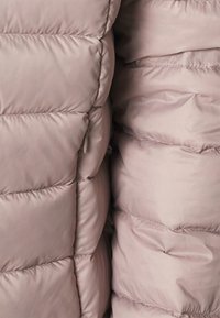 Veste gonflée rose avec un design matelassé, dotée d'un tissu lisse et brillant et d'un rembourrage épais et doux. Détail montrant les coutures et la texture.