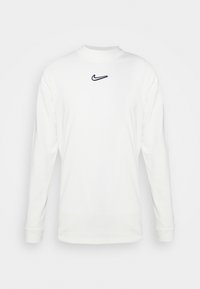 White long-sleeve shirt made from cotton with a round neck. Features a black embroidered Nike logo on the chest. Smooth texture, casual design.