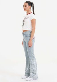 Hvid cropped t-shirt med røde kanter og grafisk print, parret med lyseblå flared jeans med hvid blomsterbroderi og en afslappet pasform.