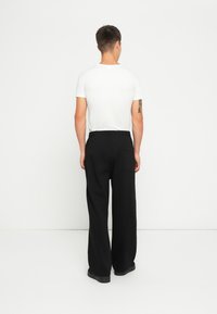Schwarze weite Hosen aus einem strukturierten Stoff mit elastischem Bund, ausgestattet mit einer Gesäßtasche und einem lockeren Sitz, getragen mit einem schlichten weißen T-Shirt.