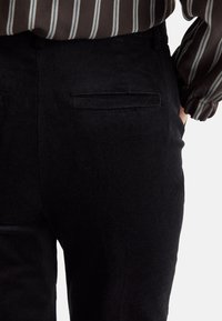 Zwarte corduroybroeken met een zachte textuur, voorzien van twee achterzakken, en gecombineerd met een bruin gestreept shirt met lange mouwen.