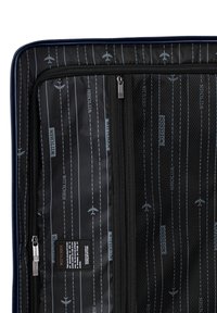 Černý interiér zavazadla s zipy a síťovými kapsami, s opakujícím se vzorem letadel a pruhů, značkový "WITTCHEN."