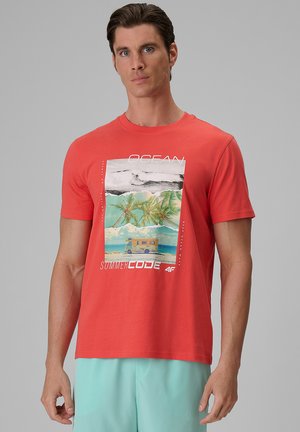 Mężczyzna w koralowym T-shircie z nadrukiem o tematyce oceanicznej, obejmującym palmy, fale, kampera i tekst "OCEAN" oraz "SUMMER CODE."