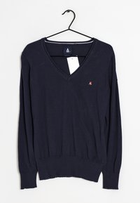 Marinblå V-ringad tröja i mjukt material, med långa ärmar och ribbat nederkant, prydd med en liten röd logotyp på bröstet. Hänger på en svart krok.