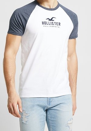 Bílý tričko s krátkými námořnickými raglánovými rukávy, na prsou s námořnickým logem Hollister California, vyrobené z měkké, lehké tkaniny.