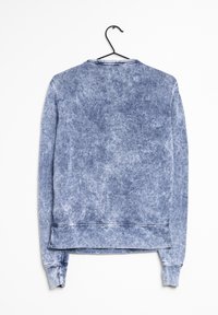 Blå sweatshirt hängande på en svart krok. Har en urtvättad, strukturerad design, långa ärmar och en rundad halslinning med en rak fåll.