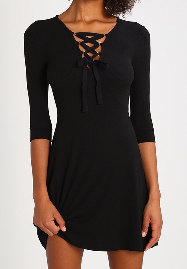 Robe noire côtelée avec un devant à lacets ornés de nœuds et accents métalliques, manches mi-longues, et un ourlet légèrement évasé.