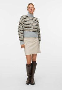 Grau gemusterter Pullover mit hohem Kragen, kombiniert mit einem beigen Leder-Minirock und braunen kniehohen Stiefeln. Strukturierte Muster auf dem Pullover.