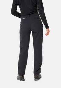 Zwarte vrouwen wandelbroeken met een gladde textuur, elastische tailleband en knienahts; gecombineerd met grijze wandelschoenen. Heeft het merklogo op de achterkant.