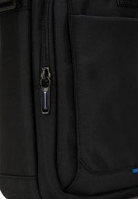 Zaino in tessuto nero con superficie testurizzata, chiusura con zip dotata di un pratico tirante, e tasca laterale con accentuazione blu.