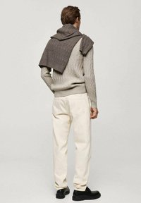 Hellgrauer Kabelstrickpullover mit einem dunkelgrauen Schal über die Schultern drapiert, kombiniert mit cremefarbenen, geraden Hosen und schwarzen Schuhen.