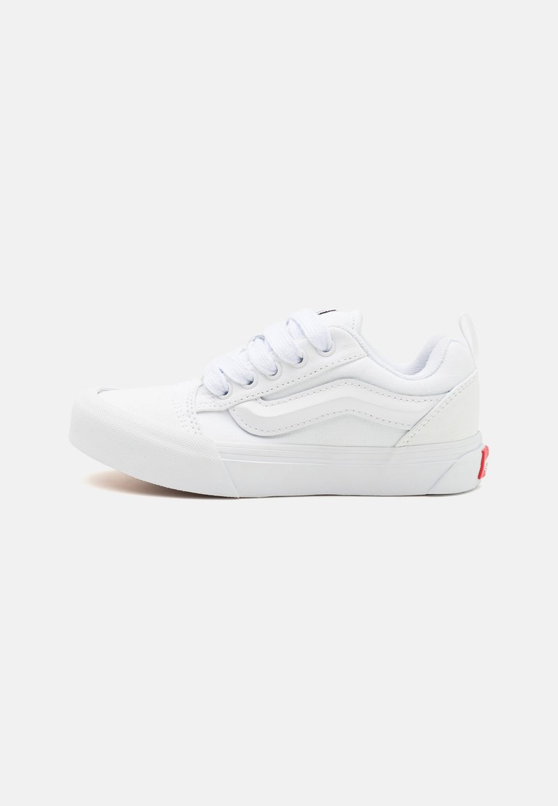Sneaker bianco basso con lacci, collo imbottito, suola in gomma e un'etichetta con logo rosso sul tallone, su uno sfondo bianco uniforme.