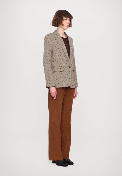 Beige blazer med sorte polkaprikker, enkelt knap, stumpe lapeller, parret med brune fløjl flared bukser og sorte hælede støvler.