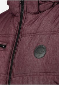 Bordeauxfarbene gesteppte Jacke mit strukturierter Oberfläche, schwarzem Reißverschluss und einem runden Lederpatch mit der Aufschrift "BLEND" auf der Brust.