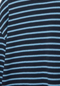 Tissu bleu marine foncé avec des rayures horizontales bleu clair régulièrement espacées, montrant un gros plan d'une section d'un vêtement.