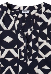 Marineblauw blouse met geometrisch crème en beige patroon, V-hals en drie knopen sluiting. Gemaakt van een gladde stof met een glanzende afwerking.
