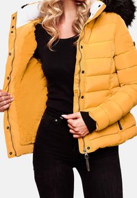 Giacca a vento gialla con un morbido rivestimento interno, chiusura con zip e polsini a coste neri. Presenta un colletto bianco e un cappuccio foderato in pelliccia.