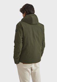 Giacca con cappuccio verde oliva dal finish opaco morbido, con chiusura con zip e tasche laterali, vista da dietro.