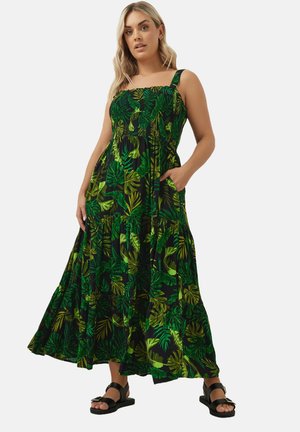 Robe maxi noire avec motif de feuilles vertes, dotée d'un corsage froncé, de bretelles larges et d'une jupe évasée à volants. Portée avec des sandales noires.