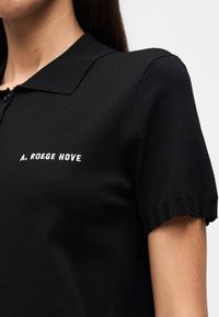 Μαύρο πλεκτό πόλο πουκάμισο με κλασικό γιακά, ριμπ κοντά μανίκια και λευκό κεντητό λογότυπο στο αριστερό στήθος.