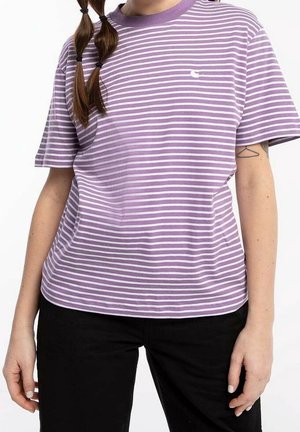 Kvinde iført en lilla og hvidstribet kortærmet skjorte med sorte bukser, der viser en geometrisk tatovering på sin venstre arm.