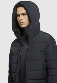 Mørkeblå dunjakke med en stor hætte, quiltet design og lynlåslommer. Fremstillet af vandafvisende materiale med en frontlynlås.