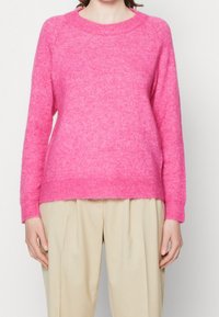 Ljusrosafärgad ullblandad tröja med rundad halsringning, raglanärmar och ribbade muddarna. Mjuk textur med en något lös passform. Matchas med beiga byxor.