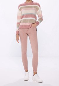 Pletený svetr s horizontálními pruhy v růžové, béžové a modré barvě; kombinovaný s růžovými skinny džíny a bílými teniskami. Útulná textura a uvolněný střih.